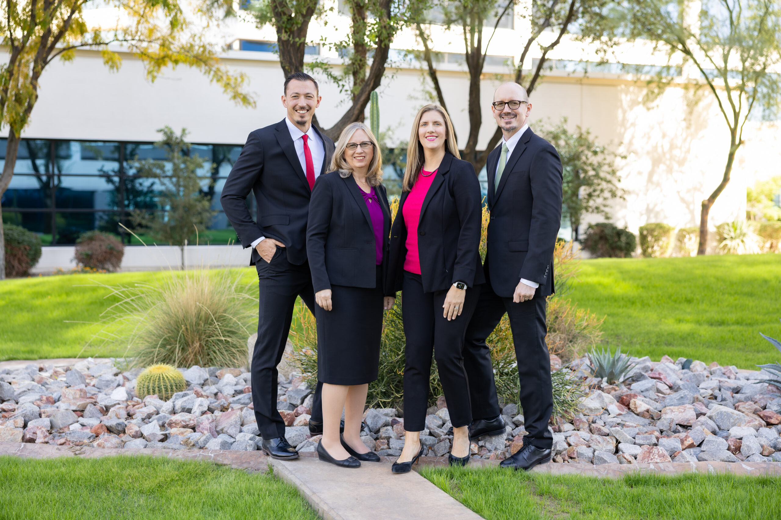 Four attorneys standing in front of a law office under a tree with grass around them and the law building in the background.