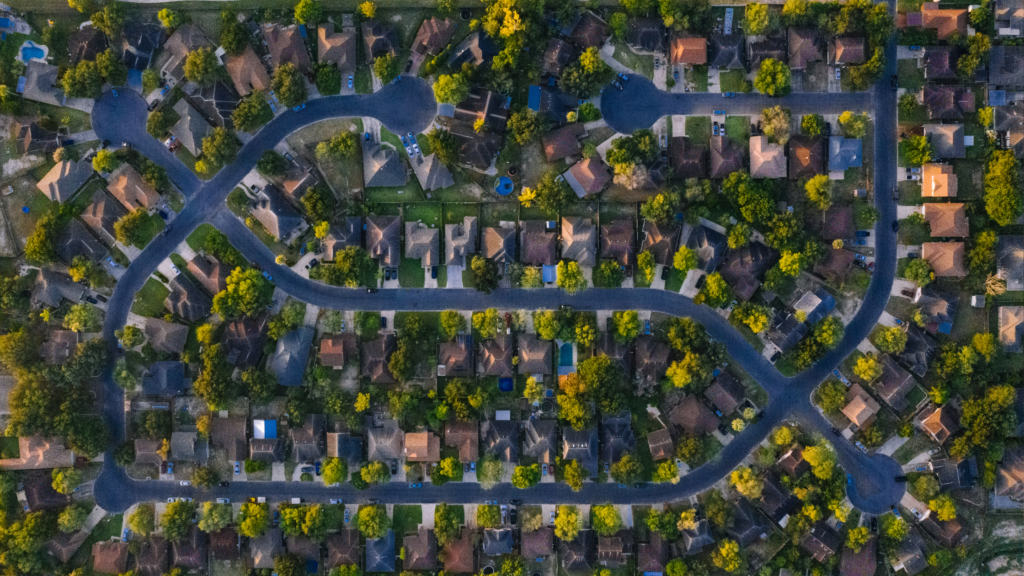 Arial view of a homeowners association filled with trees, houses, yards and winding roads.